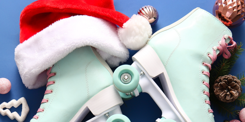 A festive image featuring a pair of light blue roller skates with pink laces, a red and white Santa hat draped over one skate, and holiday ornaments, pinecones, and greenery arranged around the skates on a blue background. 