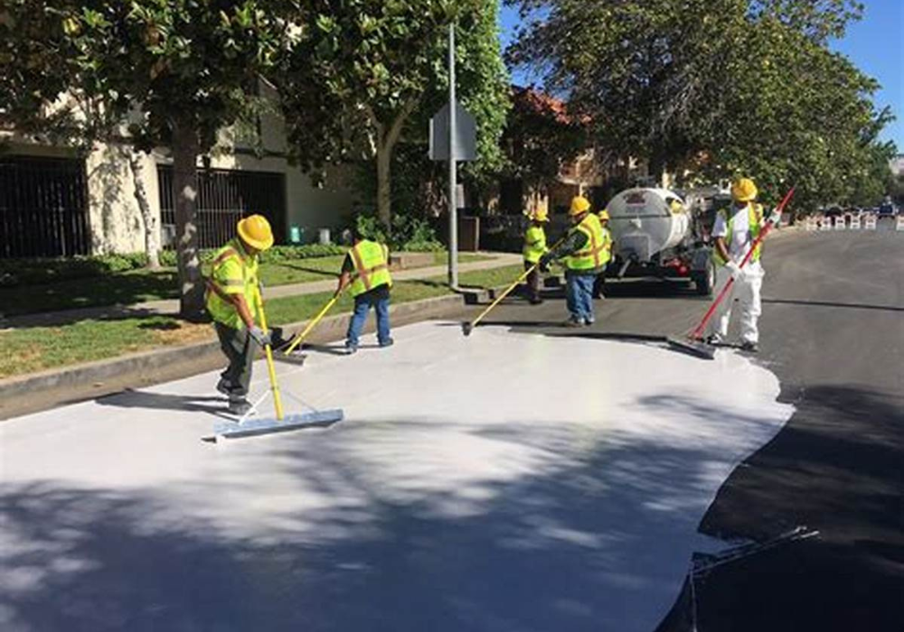 Construction workers applying cool pavement seal to street