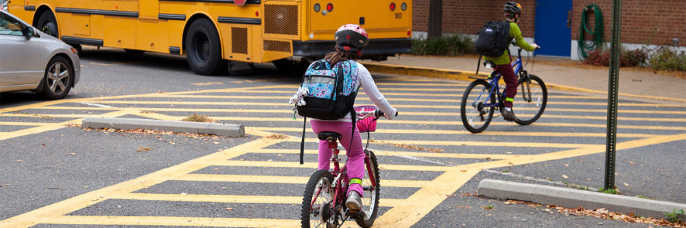 Children-ride-bicycles-outside-school-and-behind-a-parked-school-bus