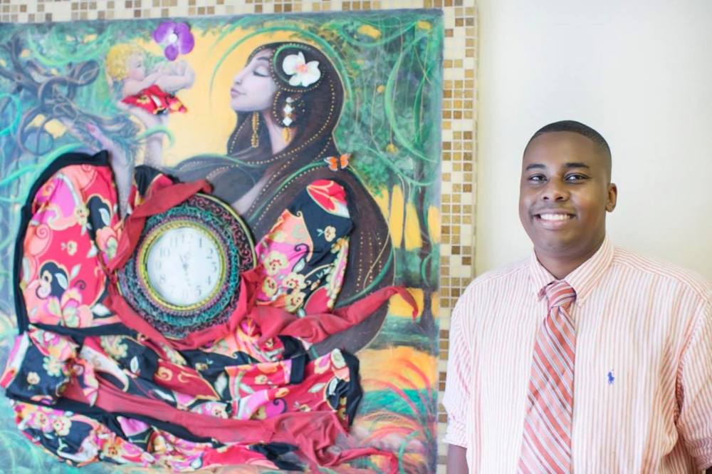 Artist Jermaine Powell is smiling and standing in front of one of his paintings