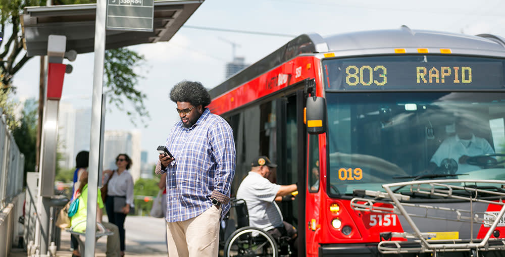 A man checks his phone in front of a MetroRapid bus.