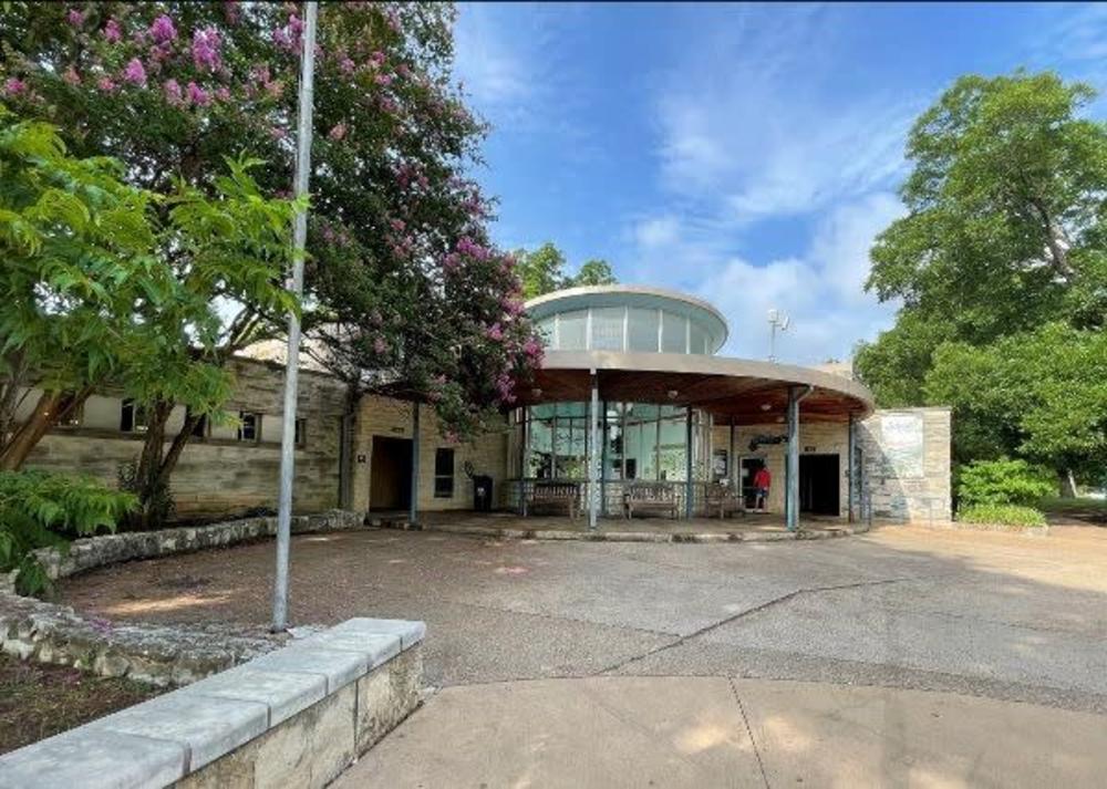 Image looking at the front of the Barton Springs Bathhouse with trees surrounding the old entrance