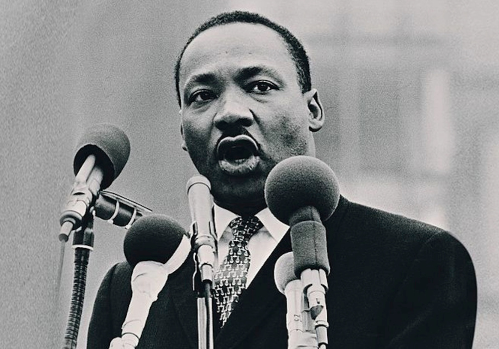 Black and white image of Dr. Martin Luther King, Jr. speaking in front of several microphones