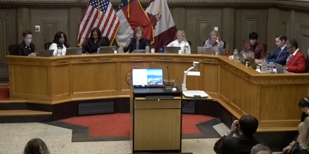 A photo of the Asheville City Council in session, with council members seated at a semicircular wooden desk.