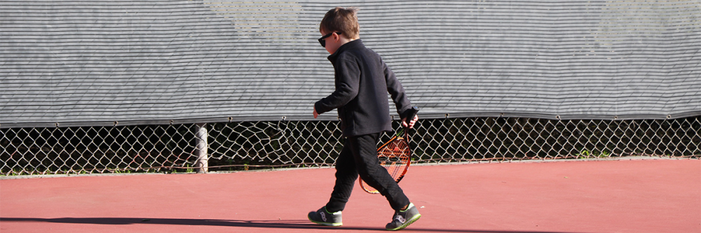 child-tennis-player-walks-on-court-with-racquet