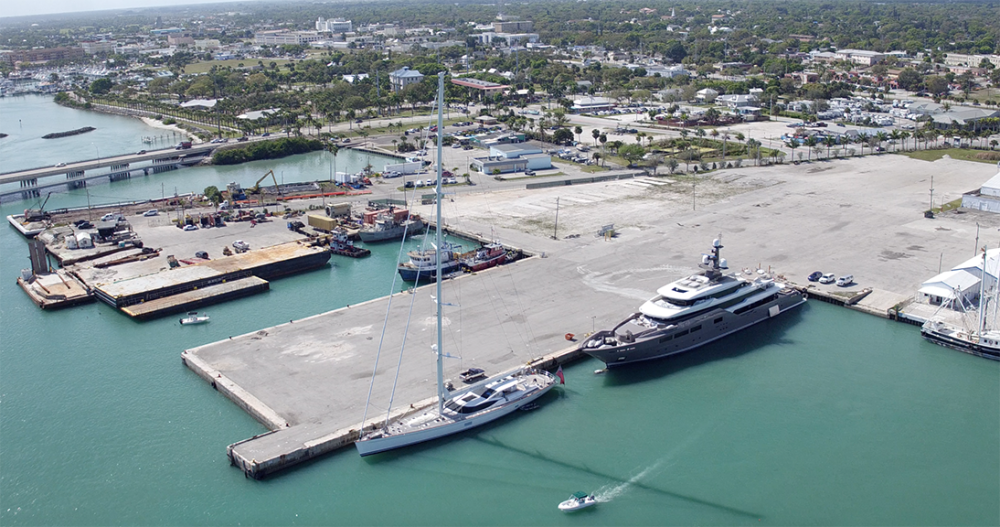 This image shows the Derektor Shipyard from the perspective of the water looking back over the project site. The port is flanked by two mega yachts and existing infrastructure surrounding the port.