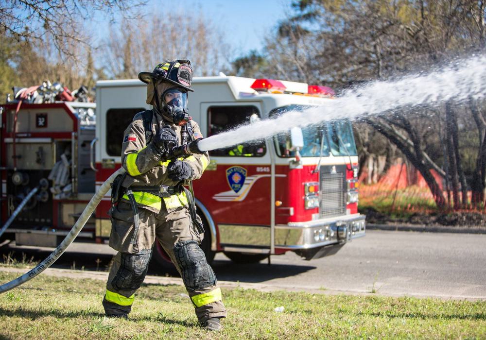 Firefighter spraying water in front of fire truck