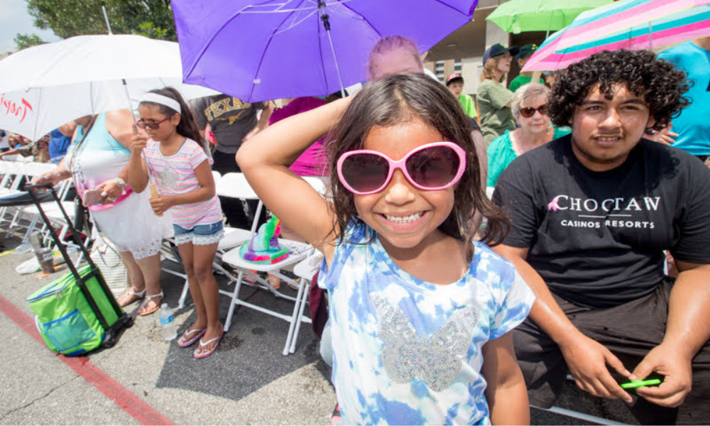 Young girl with glasses smiles at the camera during a parade