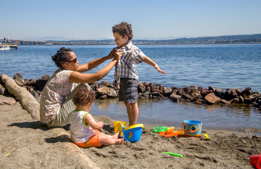 Foto: mujer cuida a dos niños pequeños en la costa. Subtítulo: Hacer las inversiones correctas en el momento correcto para lograr los mejores resultados en cuanto a la calidad del agua.