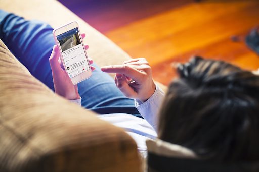 person laying on couch scrolling on smartphone